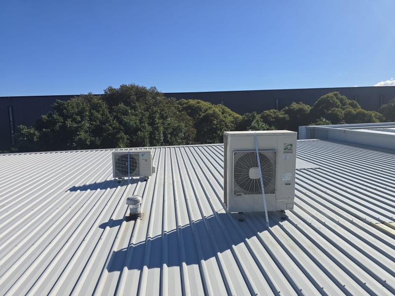 Two outdoor air conditioning condensers installed on a commercial metal roof under a clear blue sky