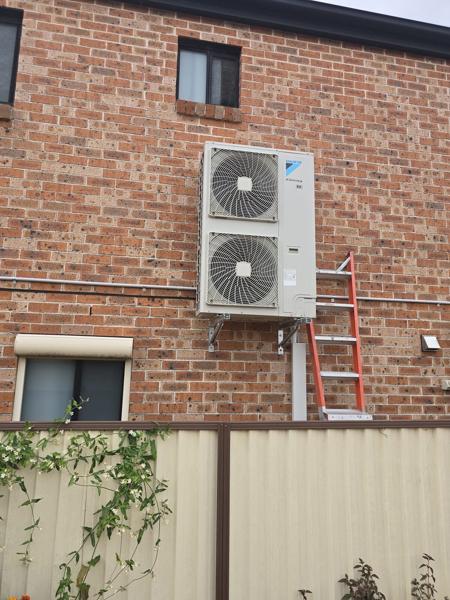 Two outdoor units bracketed one above the other on a double-storey brick wall