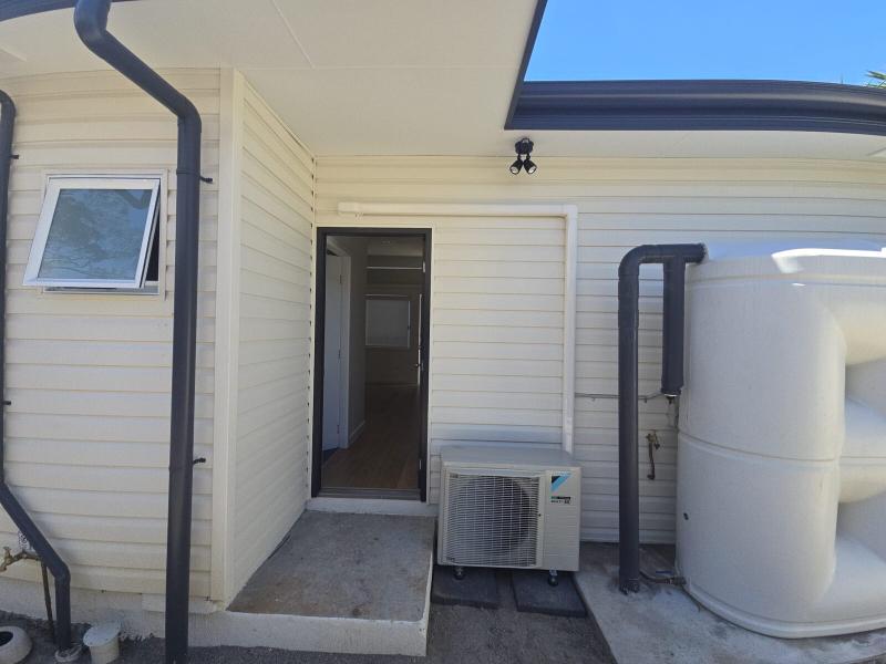 Outdoor condenser installed in a narrow side access path next to a hot water tank