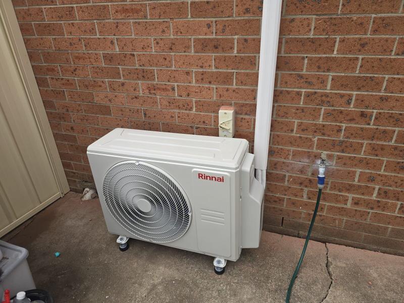 Ground-mounted outdoor condenser against a brick wall with weatherproofed connections