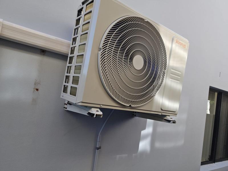 Air conditioning condenser mounted on a steel wall bracket above ground level